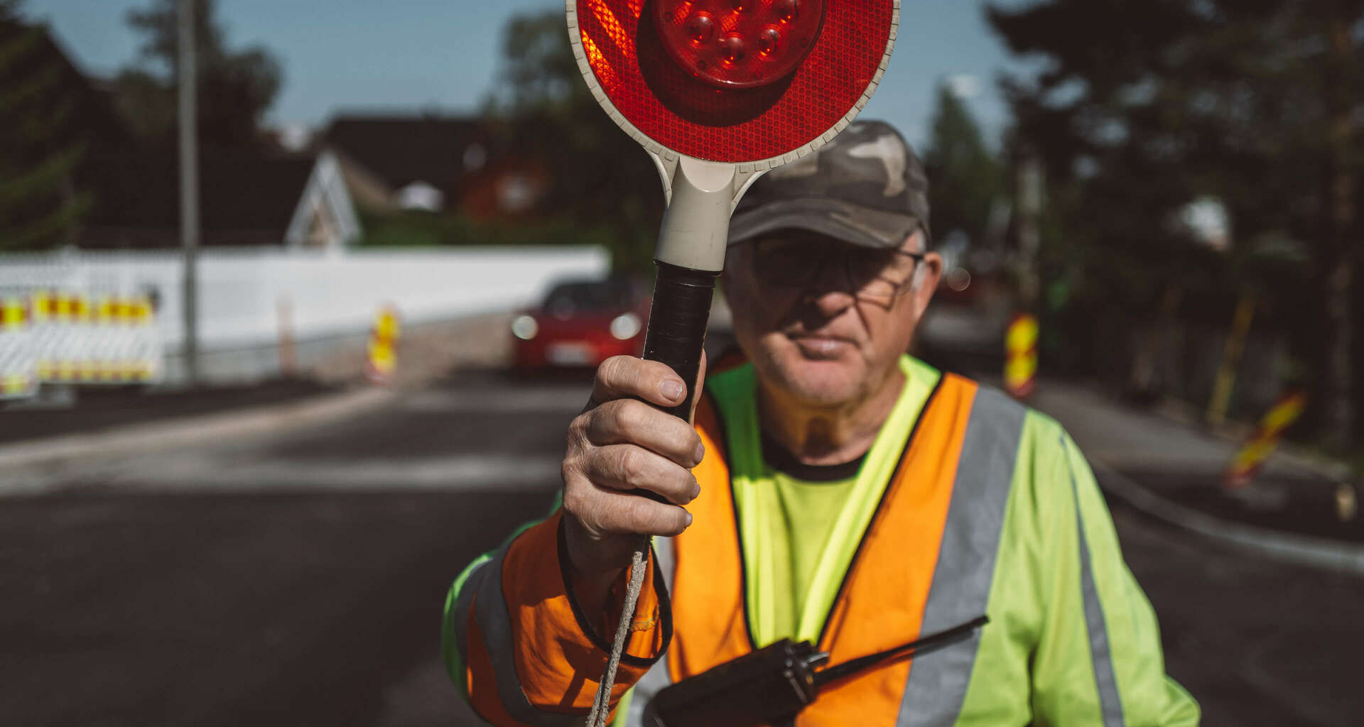 Eldre mann i gul vest som står med stoppskilt for å dirigere trafikk. Foto