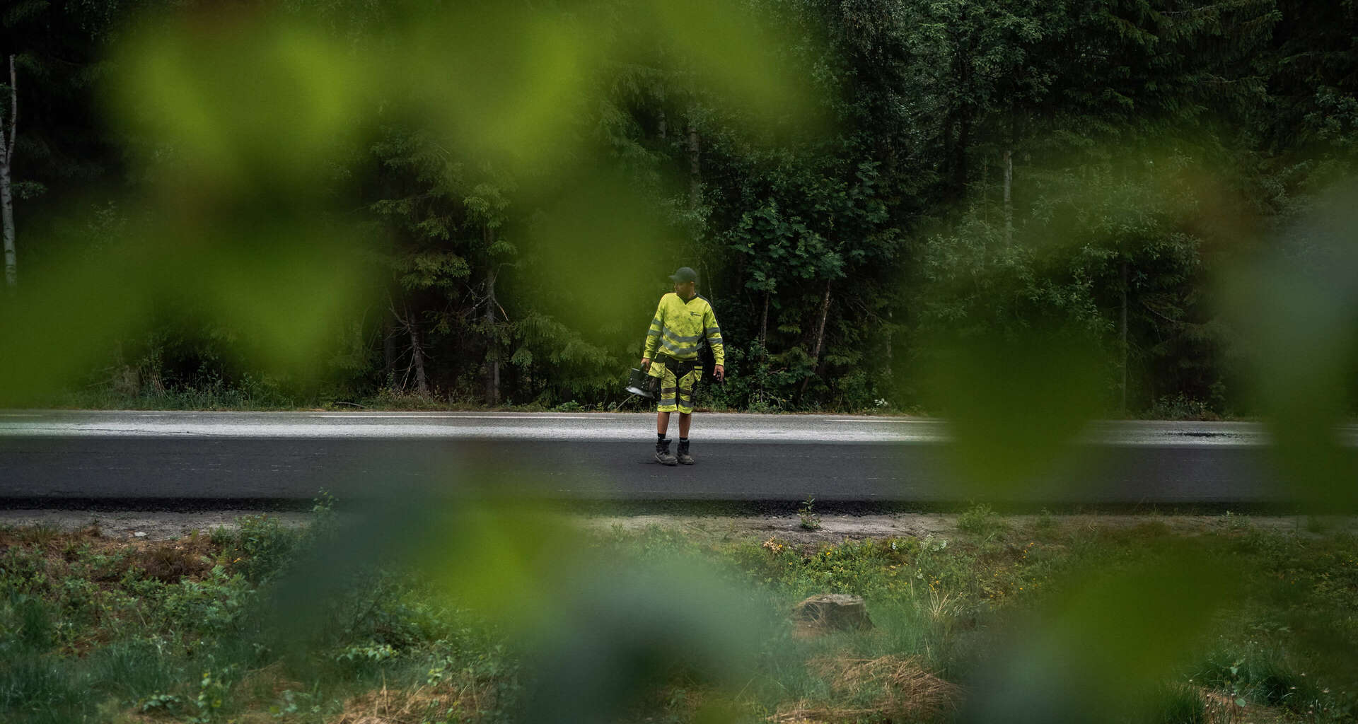 Ansatt hos Brani som står med måleinstrument på nyasfaltert vei midt i skogen. Foto